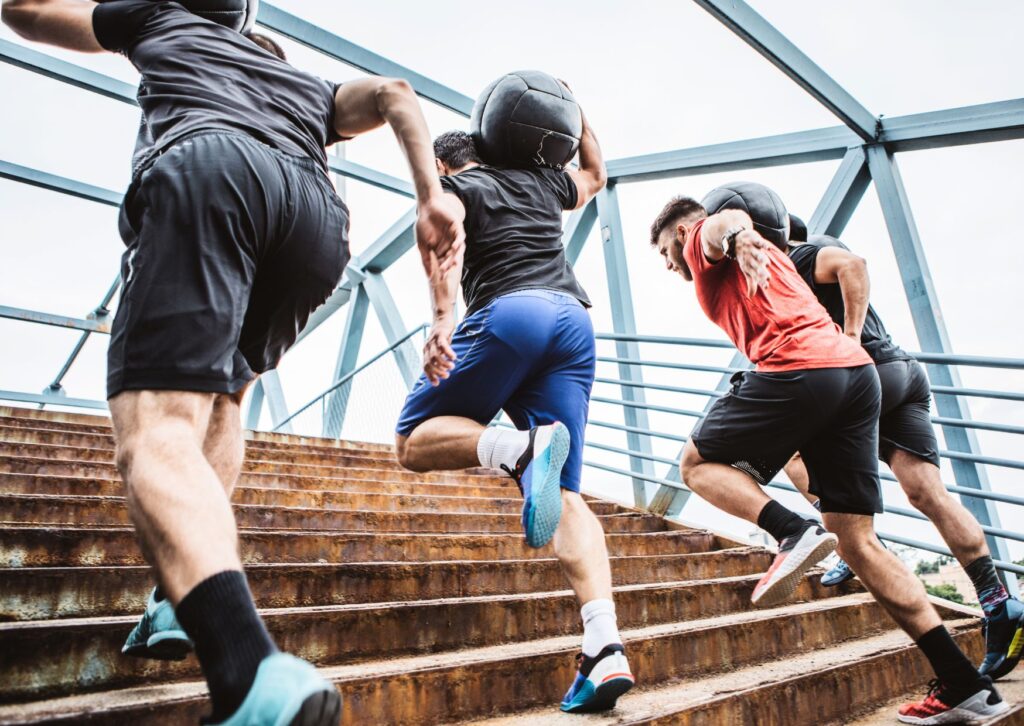 men-taking-part-in-a-corportae-fitness-challenge-carrying-weighted-balls-up-stairs